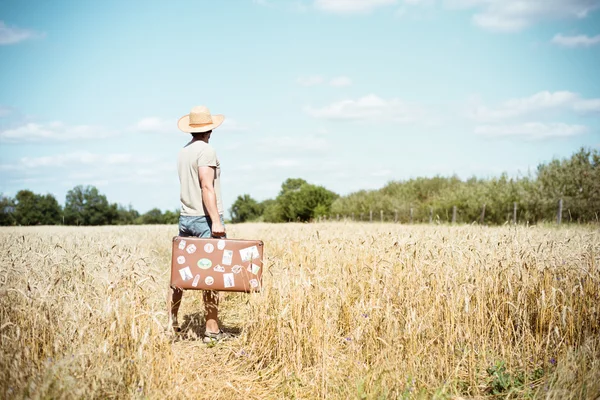 Man in straw hat holding old suitcase in wheat field — 图库照片