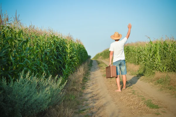 Back view of travel man holding suitcase on country road — Stockfoto