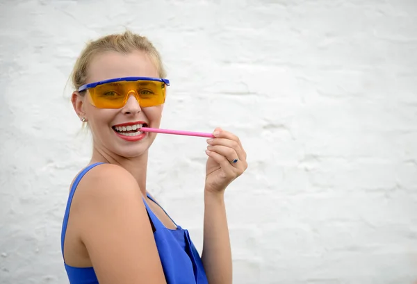 Beautiful young exciting lady in glasses biting pencil beside white wall — Stock Photo, Image