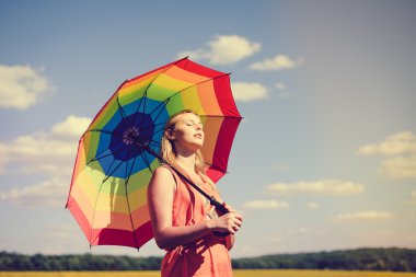 Beautiful joyful young female with rainbow umbrella sunning in summer countryside