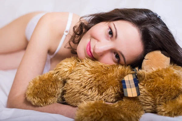 Joyful beautiful young woman in white underwear lying with teddy bear — Φωτογραφία Αρχείου