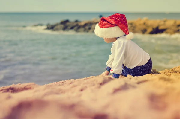 Backview of little kid in Santa hat on sunny seaside — ストック写真