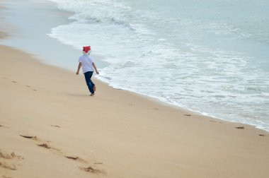 Backview of kid in Santa hat running on sunny seashore