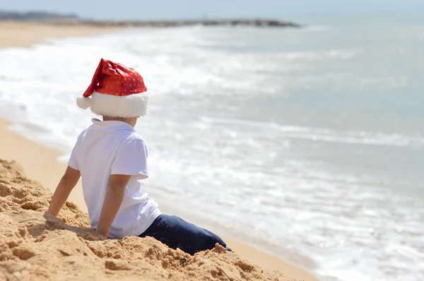 Маленький мальчик в красной шляпе, смотрит на океанские волны — стоковое фото