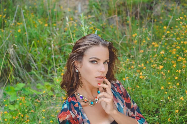 Beautiful young lady in fancy necklace sitting in countryside wildflowers — Stockfoto