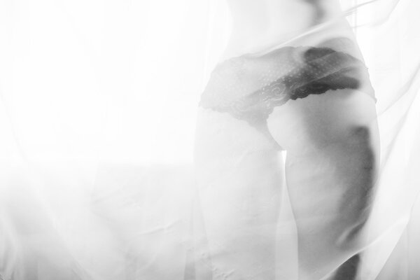 Glamor sexy girl with excellent fitness buttocks having fun happy standing back to camera over window light copy space background. Closeup black and white photography