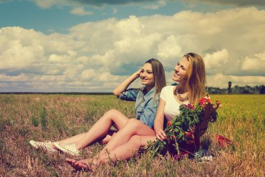 Two beautiful young ladies sitting with flowers on summer meadow
