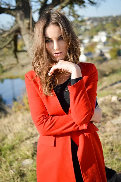 Schöne junge Frau im eleganten roten Mantel in der herbstlichen Landschaft — Stockfoto