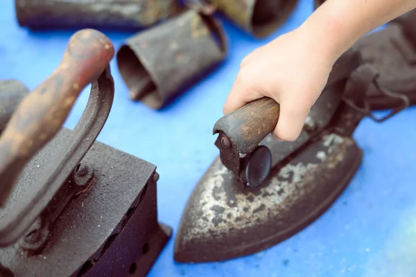 Hand holding old rusty obsolete iron standing on blue tabletop — Stok fotoğraf