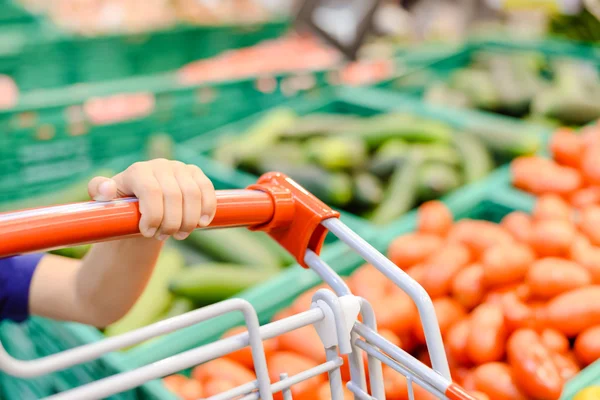 Carretto maniglia rosso con mano ragazzi accanto display verdura negozio — Foto Stock