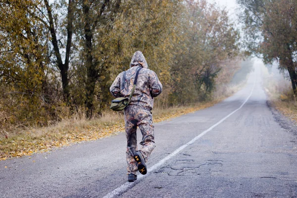 Зворотній бік людини в камуфляжі, що працює на осінній сільській дорозі — стокове фото