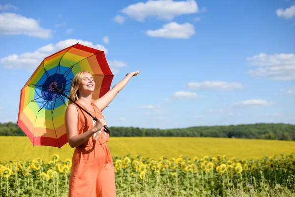 Beautiful young woman with rainbow umbrella beside summer sunflowers field — Stock Photo, Image