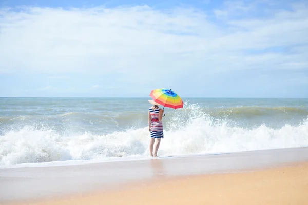 レインボー傘の日当たりの良い海岸の上を歩くと美しい若い女性 — ストック写真