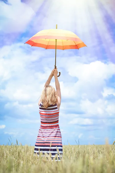 Beautiful young woman rising colorful umbrella on golden wheat field — Stock Photo, Image