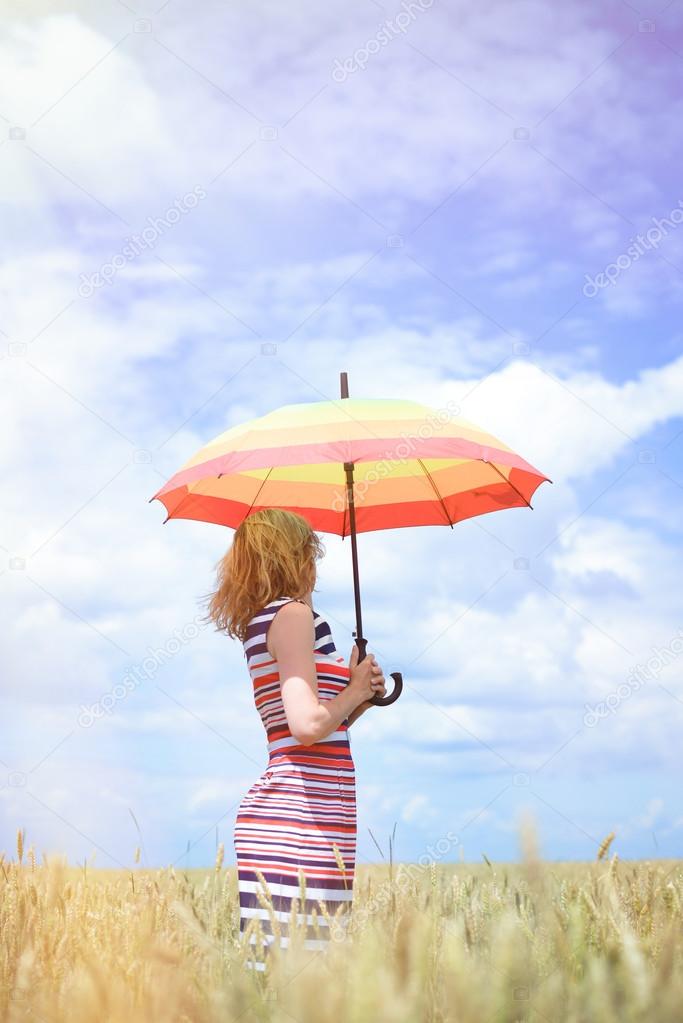 Beautiful young female standing with colorful umbrella on wheat field