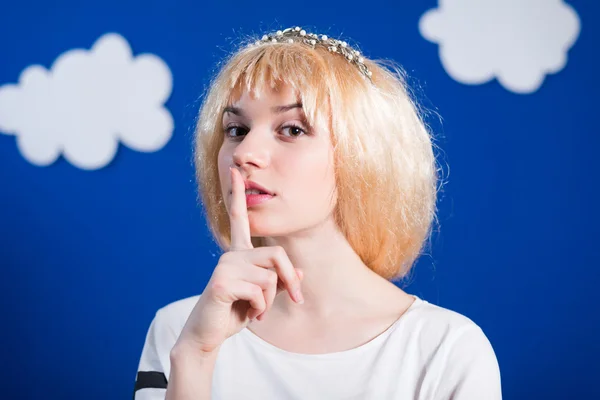 Beautiful young lady in golden wig shushing beside paper clouds — Stock Photo, Image