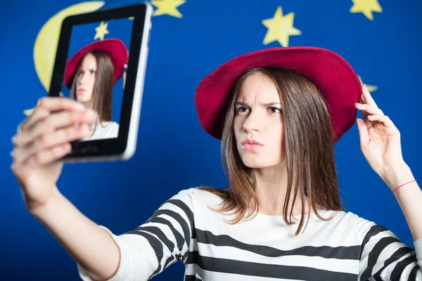 Schöne junge Frau macht Selfie und runzelt auf blauem Bildschirm die Stirn — Stockfoto