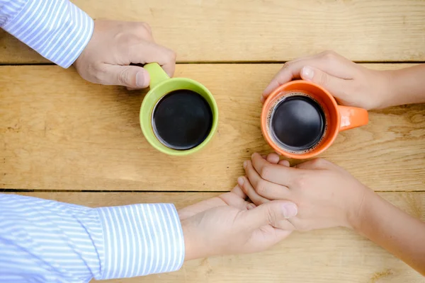 Closeup of couple holding hands with coffee mugs on table — 스톡 사진