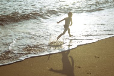 Little boy running on beach beside waves in evening sunlights