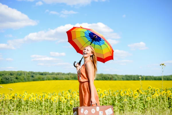 Schöne junge Dame mit Regenschirm und Koffer neben Sonnenblumenfeld — Stockfoto