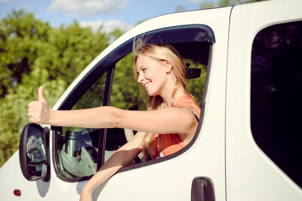 Beautiful young female looking from white car window and thumbing — ストック写真