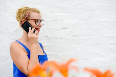 Beautiful young lady in big glasses speaking phone in garden