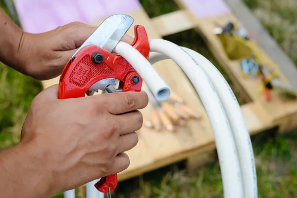 Zbliżenie mężczyzna ręce cięcia plastikowe rury nożycami czerwony — Zdjęcie stockowe