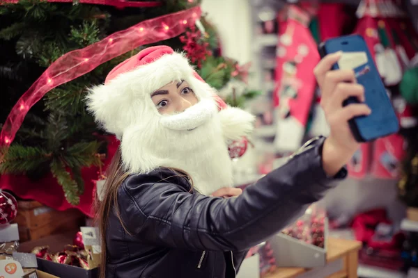 Bella giovane donna che indossa il costume di Babbo Natale facendo selfie in negozio — Foto Stock