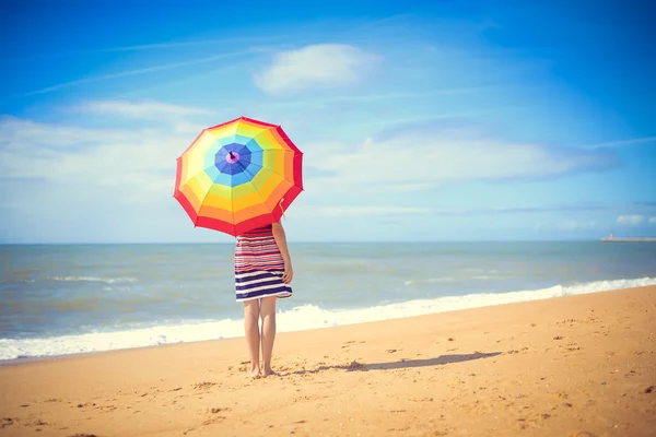 Belle jeune femme derrière grand parapluie arc-en-ciel sur le bord de mer doré Photo De Stock