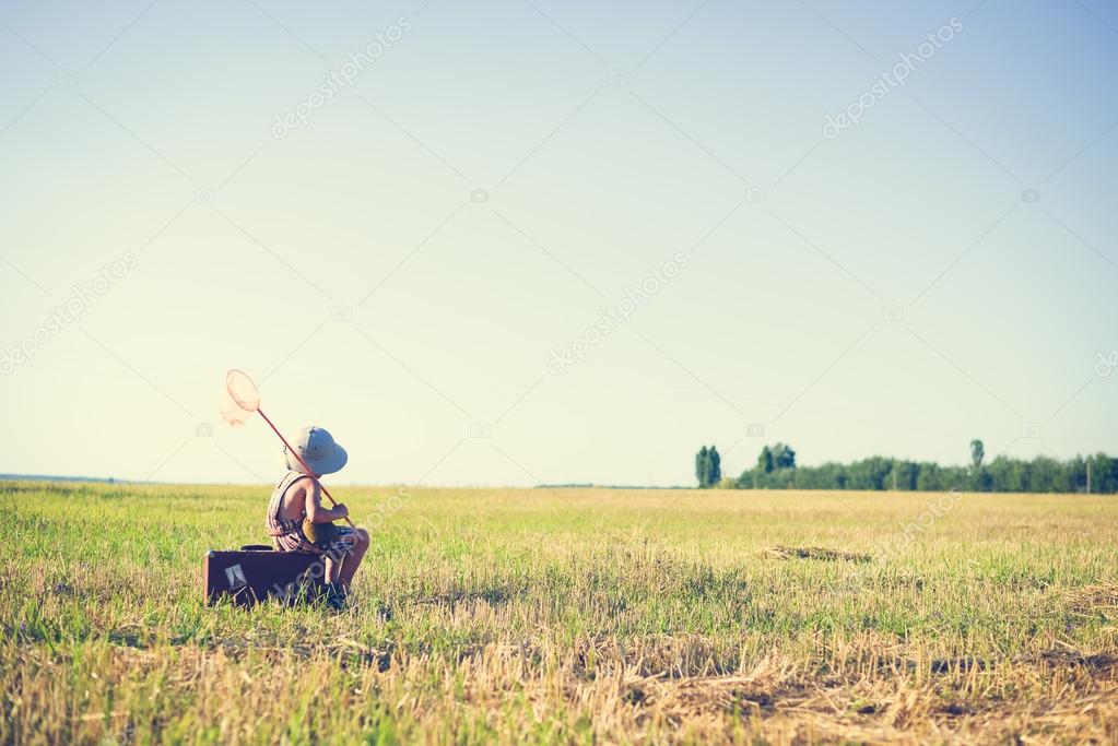 Little boy sitting on old suitcase with insect-net in countryside