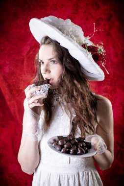 Beautiful young lady in retro clothes eating chocolate on red copy space background and looking forward