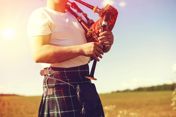 young man playing pipes in national uniform on green summer outdoors copy space background, closeup picture