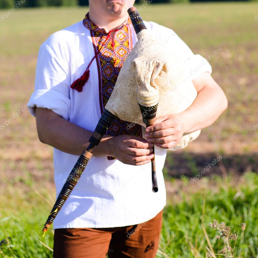 Portrait of man enjoying playing pipes in Ukrainian traditional shirt on green outdoors copy space summer field