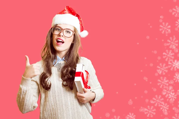 Picture of showing thumb up and holding present box beautiful young lady in Christmas hat, glasses happy smiling and looking at camera