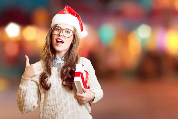 Mostrando polegar para cima e segurando presente caixa bela jovem senhora no chapéu de Natal, óculos felizes sorrindo e olhando para a câmera — Fotografia de Stock