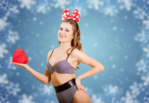 Immagine di giovane femmina attraente in costume da bagno che tiene il cuore rosso sopra i fiocchi di neve invernali sfondo astratto — Foto Stock