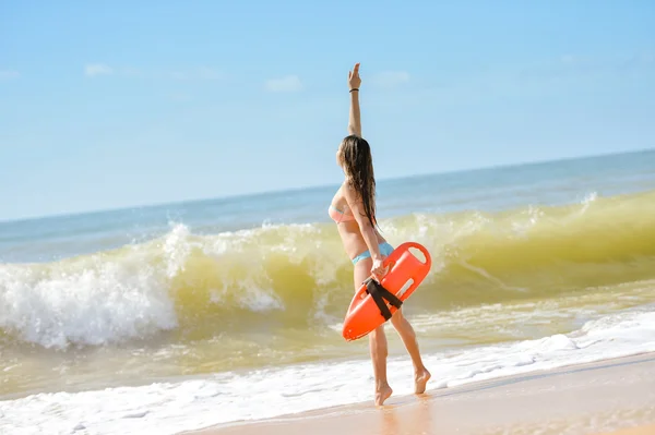 Beautiful young lady with orange lifesaver equipment beside sea waves — Stock fotografie