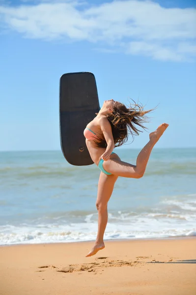 Hermosa joven bailando con tabla de surf negro para principiantes en la playa — Foto de Stock
