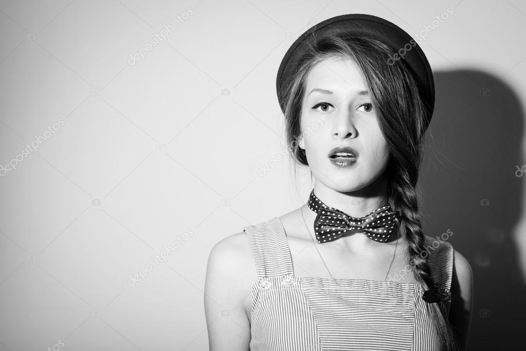 Beautiful girl in hat and bow tie looks surprised. Black and white photography