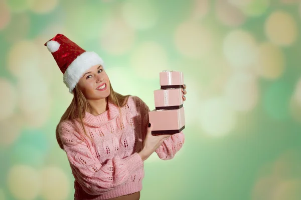 Picture of beautiful young lady in Santa red hat holding gift boxes on abstract festive design background — Stock Photo, Image