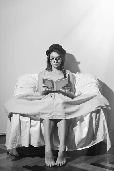 ผู้หญิงที่งดงามในหมวกโบว์ลิ่งและแว่นตาอ่านหนังสือนั่งบนโซฟาหรือเก้าอี้ . — ภาพถ่ายสต็อก