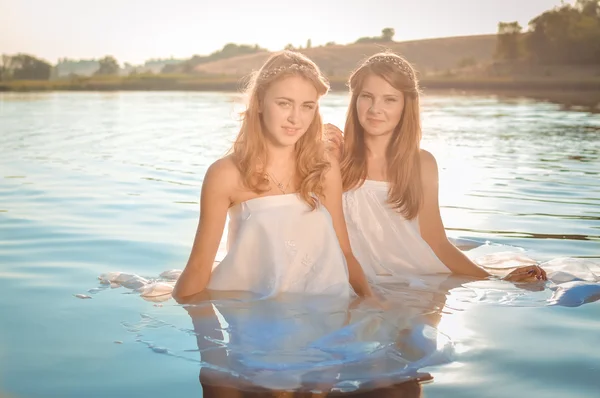 Portrait of two beautiful princess young ladies in white dresses on summer sunset water outdoors background — ストック写真