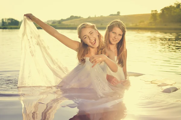 Imagem de 2 bela princesa jovens senhoras emocionantes em vestidos brancos no verão pôr do sol água ao ar livre fundo Imagem De Stock