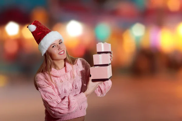 Bild der schönen jungen Dame in Weihnachtsmann roten Hut hält Geschenkboxen auf abstrakten festlichen Design Hintergrund — Stockfoto