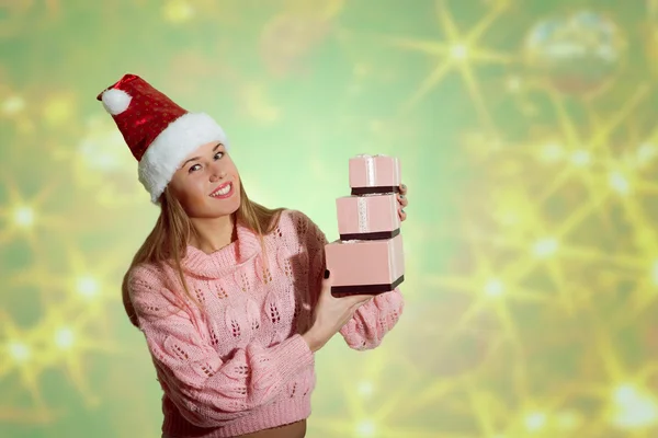 Picture of beautiful young lady in Santa red hat holding gift boxes on abstract festive design background — Stockfoto