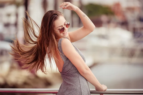 Bella eccitata giovane signora in occhiali da sole e vestito girando accanto ringhiera — Foto Stock