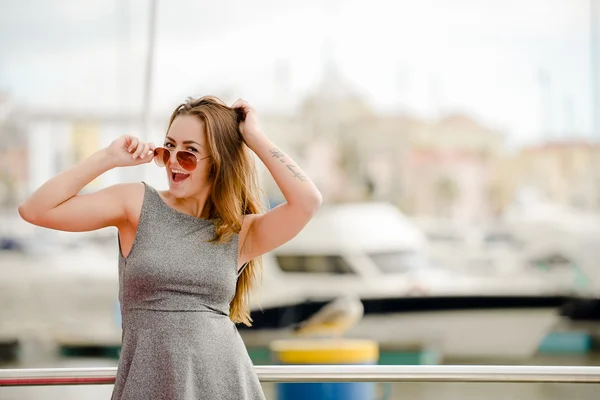 Beautiful young lady in sunglasses wearing dress standing beside railing — Stock Photo, Image