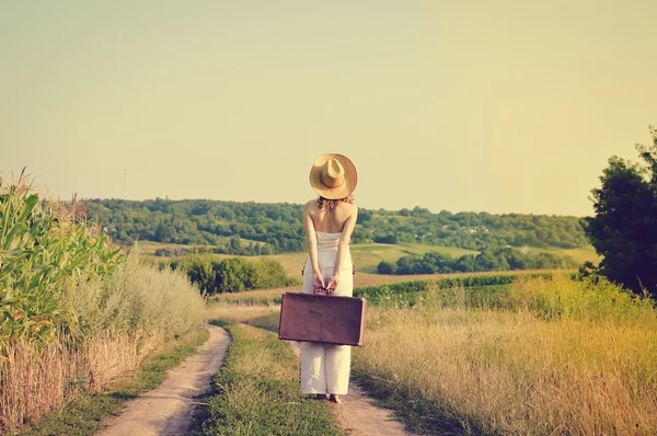 Обзор восхитительной молодой женщины с чемоданом, стоящей на проселочной дороге — стоковое фото