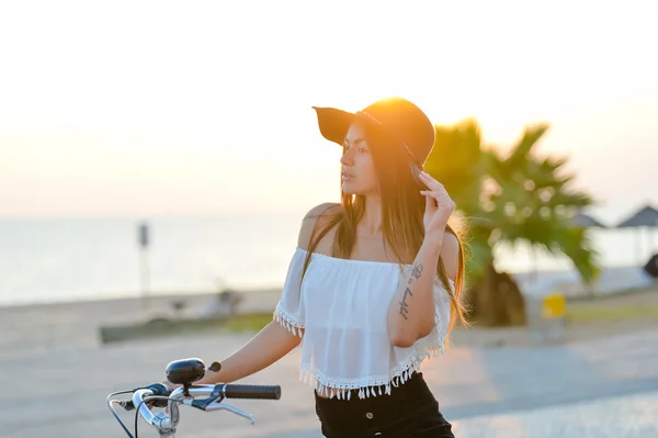 Pretty girl in black hat on bicycle looking at distance — Stock Photo, Image