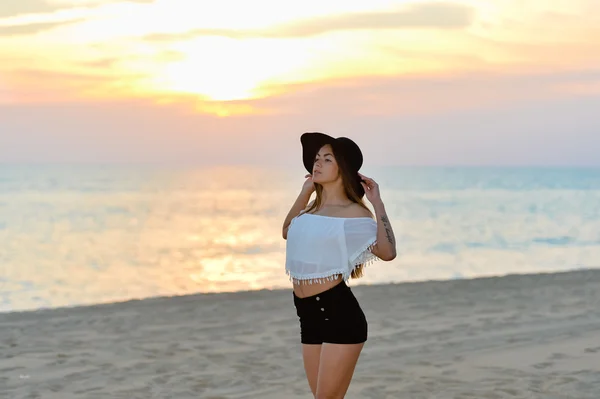 Menina bonita em chapéu preto e camisas na praia pôr do sol — Fotografia de Stock